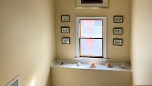 A room with a window, a shelf with decorative items, and several framed pictures on the wall. - Sunshine House - 3BR home close to everything, screen porch! No Linens (Chincoteague)