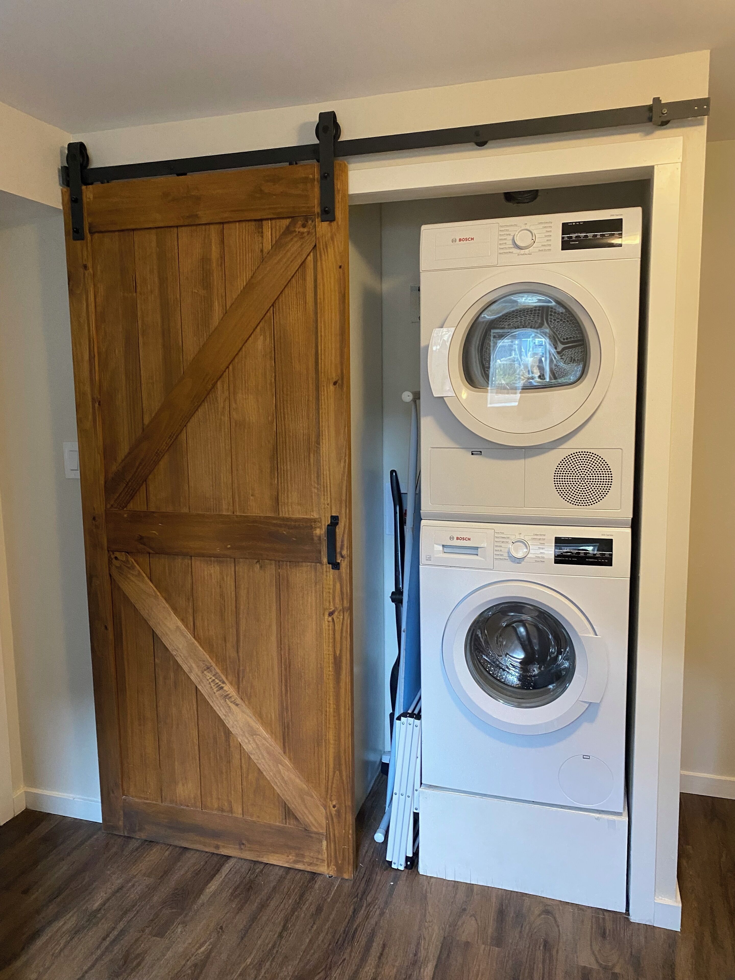 Une buanderie dotée d’une porte en bois de style grange et de deux machines à laver Bosch superposées.