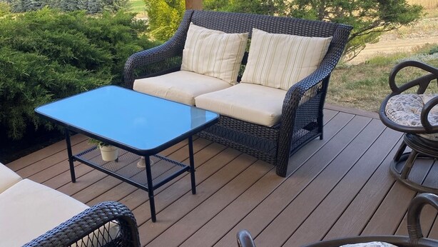 A deck with wicker furniture, including a sofa and chairs, and a glass-top table.