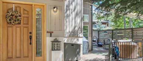 A wooden front door with a wreath, a glass panel, a lantern, and a covered outdoor seating area with a grill.