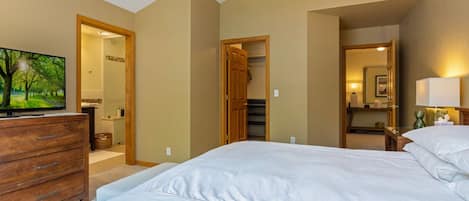Un dormitorio con una cama, un aparador de madera, un ventilador de techo y un televisor sobre un aparador.