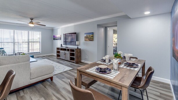 Un salon moderne avec un coin repas, comprenant une table à manger en bois pour quatre personnes, un canapé et un téléviseur posé sur un meuble.
