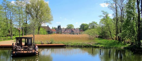 Ein ruhiger See mit einer Holzsteganlage und einem kleinen Boot, umgeben von üppigem Grün und einem Haus im Hintergrund.