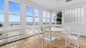 A sunroom with large windows overlooking a beach, wooden flooring, and white furniture. - Alive After Five Where Tranquility Meets the Ocean (Pawleys Island)
