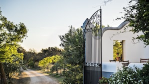 A cobblestone path leading to a gated entrance with a white building and a table with chairs outside.