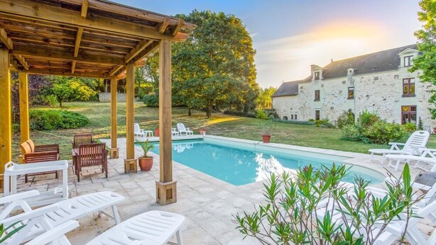 Ein Poolbereich mit Liegestühlen, einer Pergola und einem Steingebäude im Hintergrund.