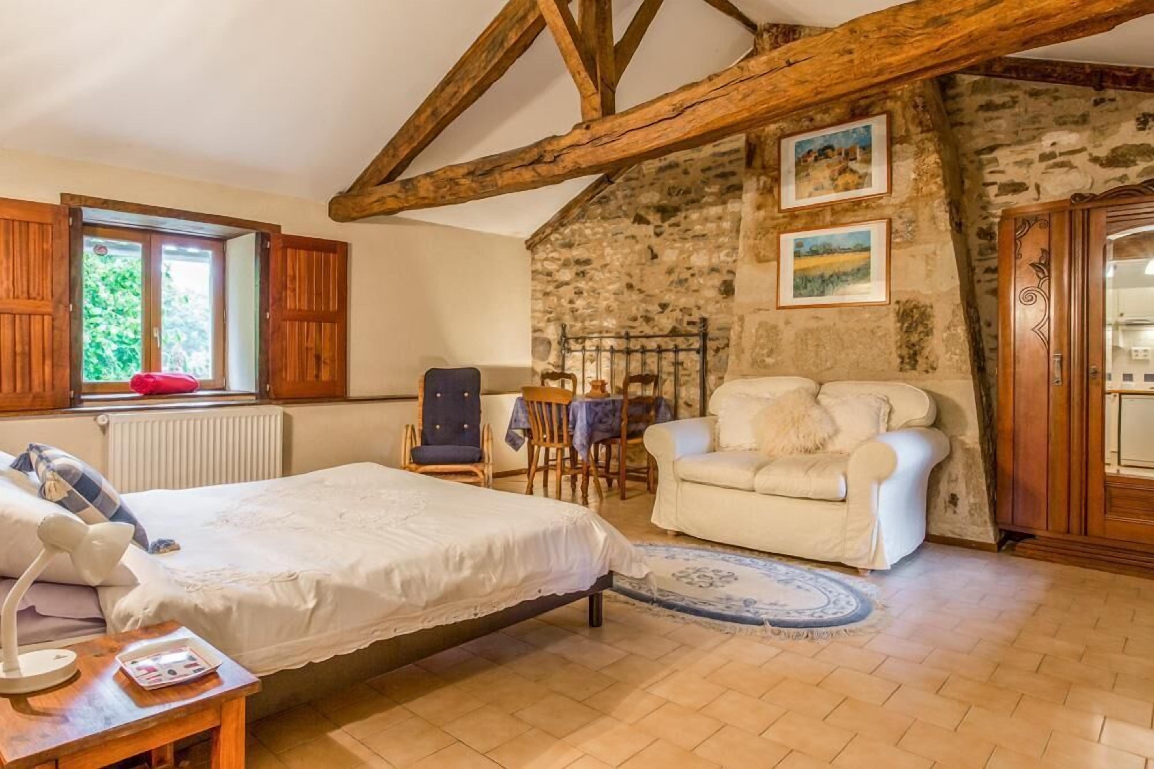 Une chambre à coucher avec un lit, une chaise, une table et une fenêtre avec des volets en bois.