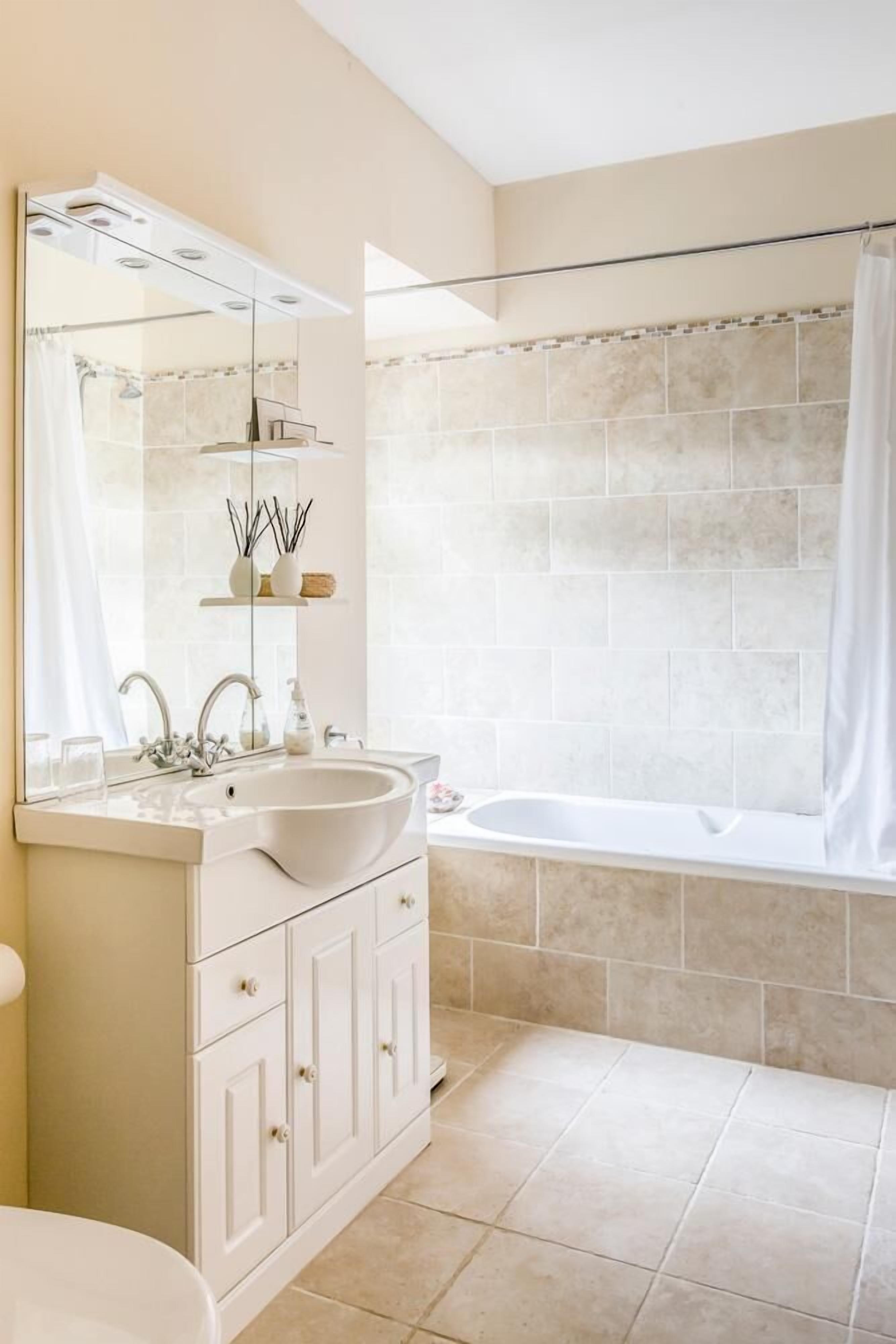 A bathroom with a white sink, mirror, and vanity, a bathtub, and beige tiled walls.