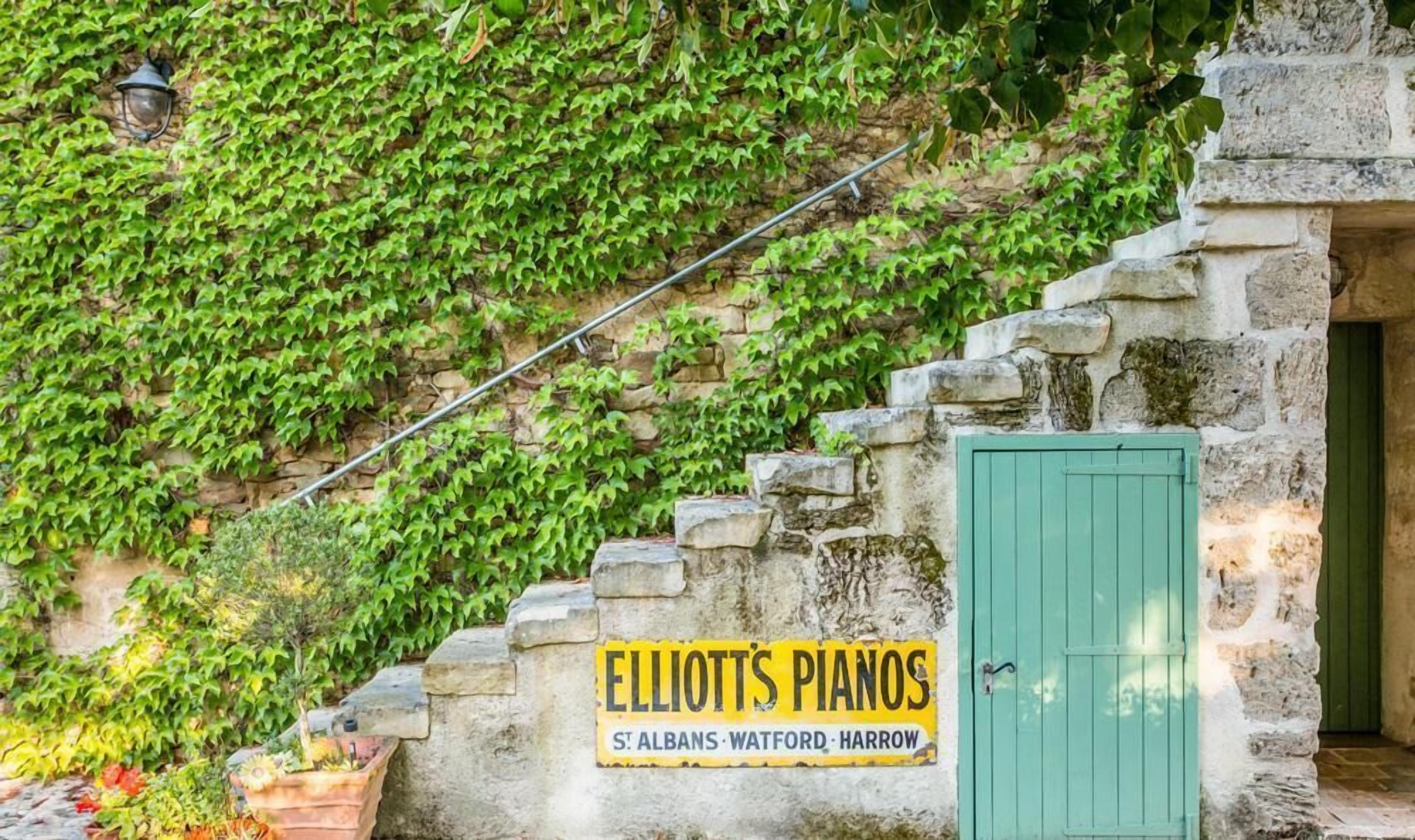 En stenmur med en skylt som visar vägen till Elliott’s Pianos i St. Albans, Watford och Harrow.