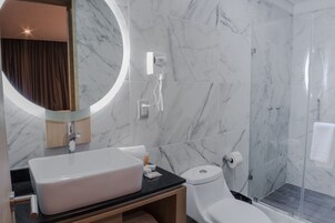 Casa de banho moderna com um espelho grande, lavatório branco, sanita e cabine de duche com parede de vidro.