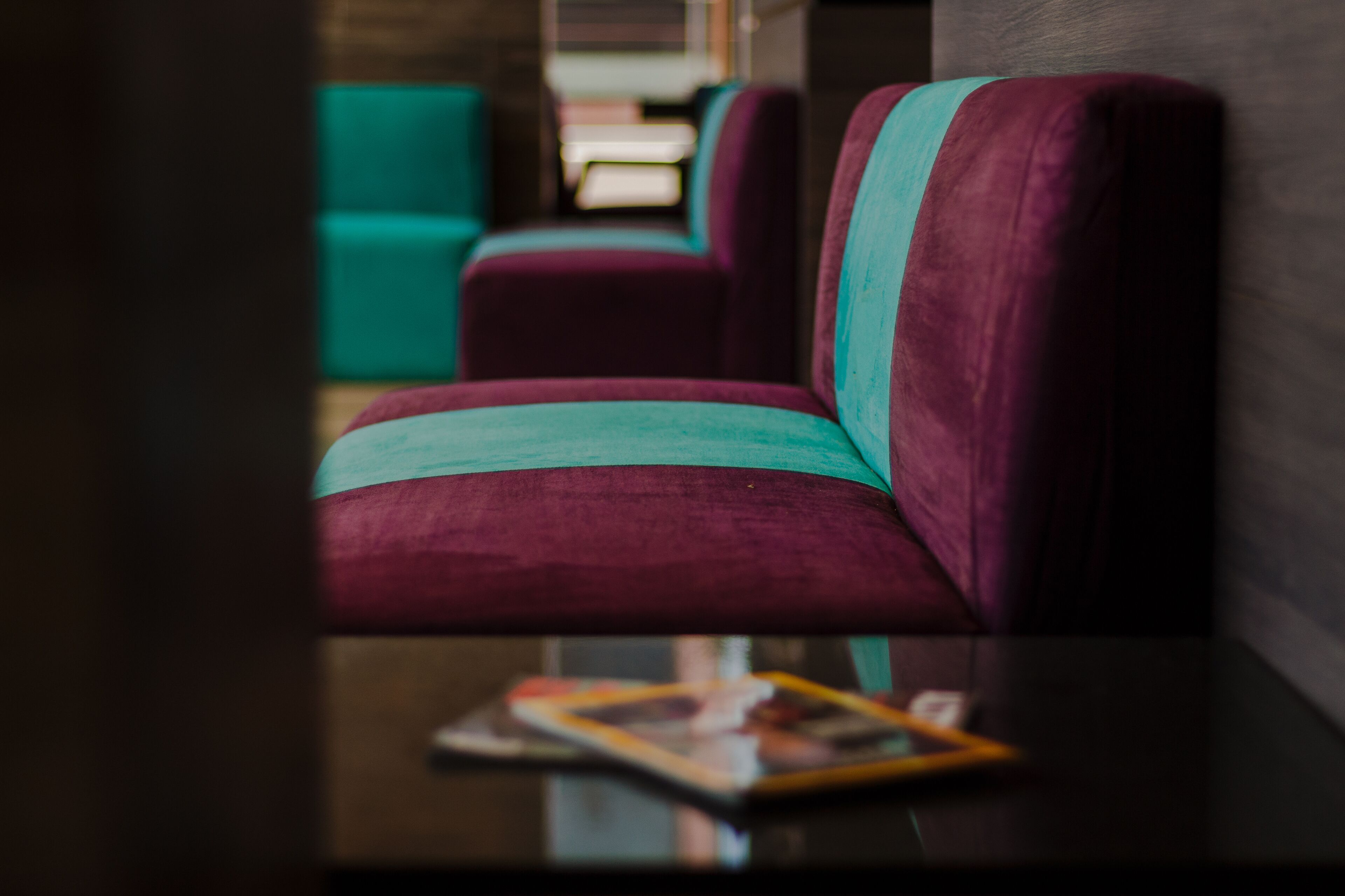Gros plan d’un fauteuil violet et turquoise recouvert d’un tissu, avec un magazine posé sur une surface réfléchissante.