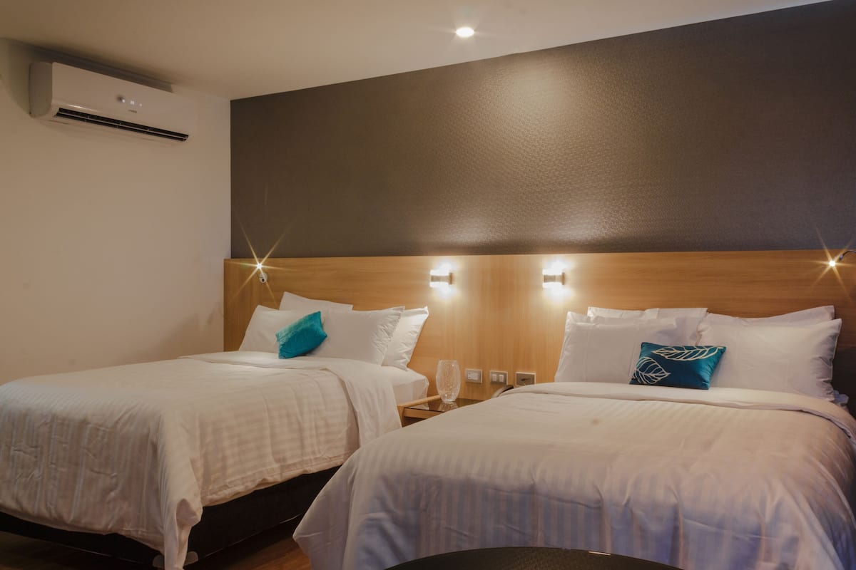 A hotel room with two beds, each with a wooden headboard, white bedding, and a nightstand with a lamp.