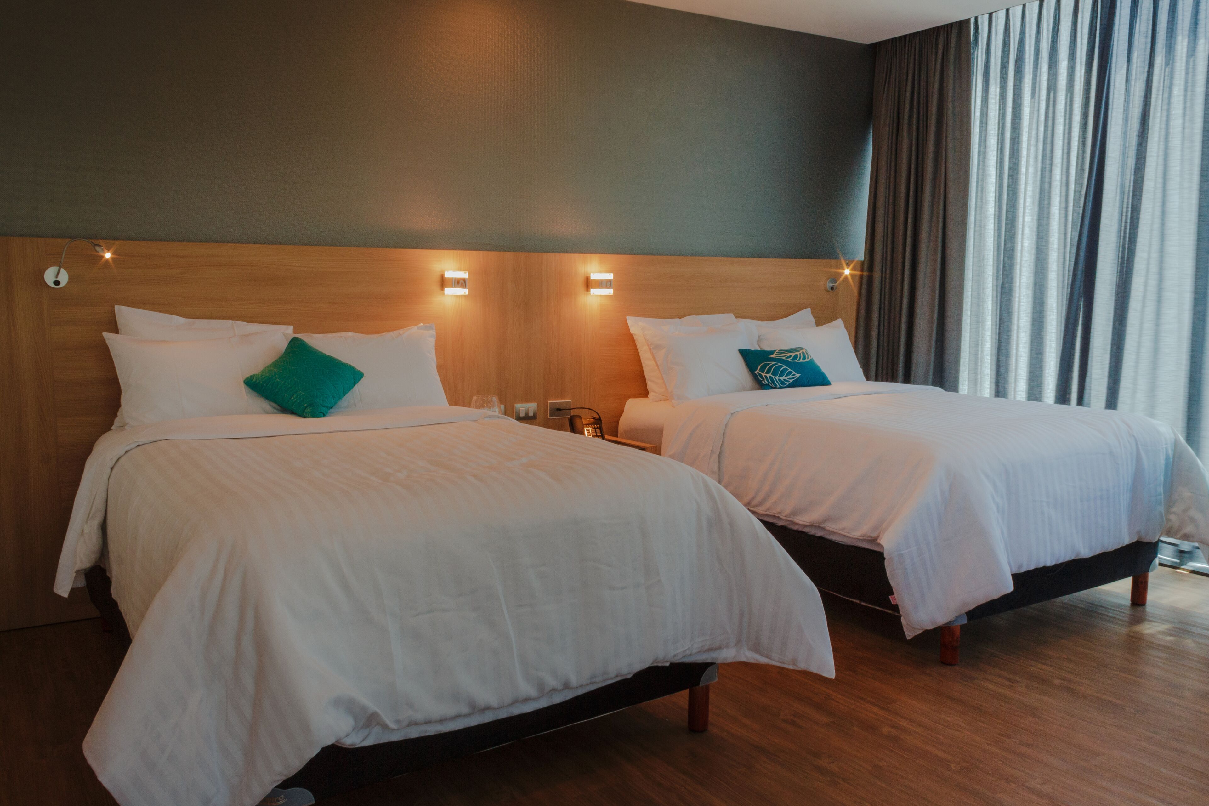 Dos camas individuales con ropa de cama blanca, cabeceros de madera y lámparas de noche.