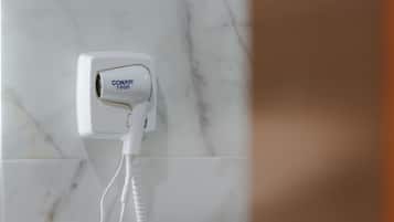 A white hair dryer plugged into a wall socket on a marble-tiled wall.