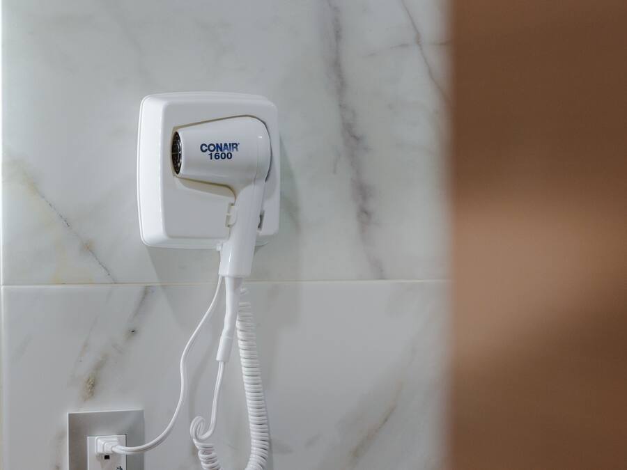 A white hair dryer plugged into a wall socket on a marble-tiled wall.