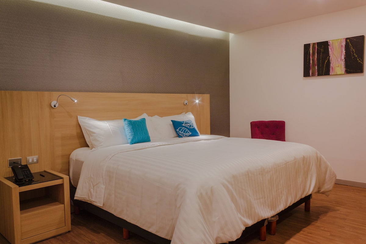 A neatly made bed with a wooden headboard, a bedside table with a phone, and a painting on the wall.