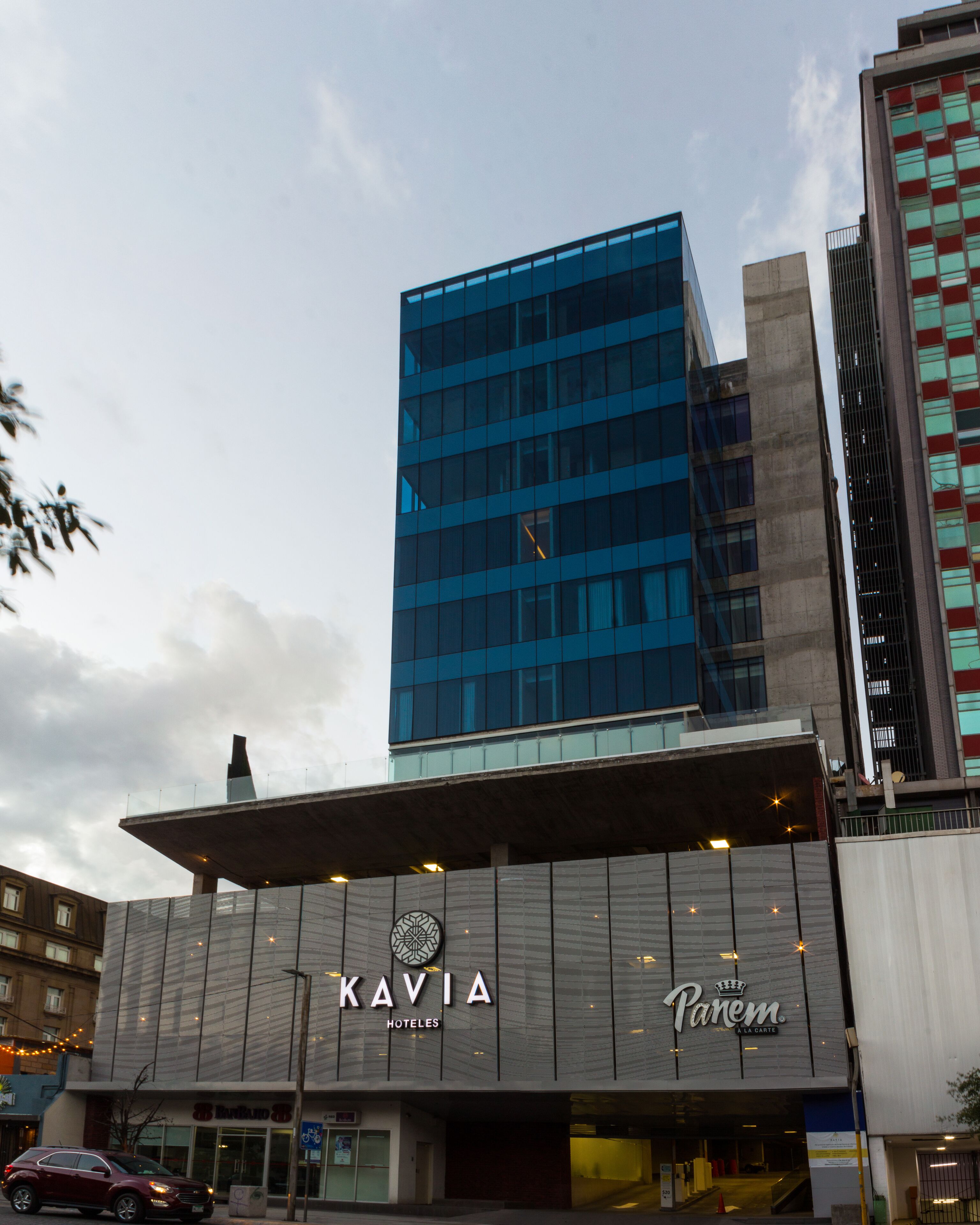 A modern hotel building with a prominent glass facade and signage for 'KAVIA HOTELES' and 'Panem'.
