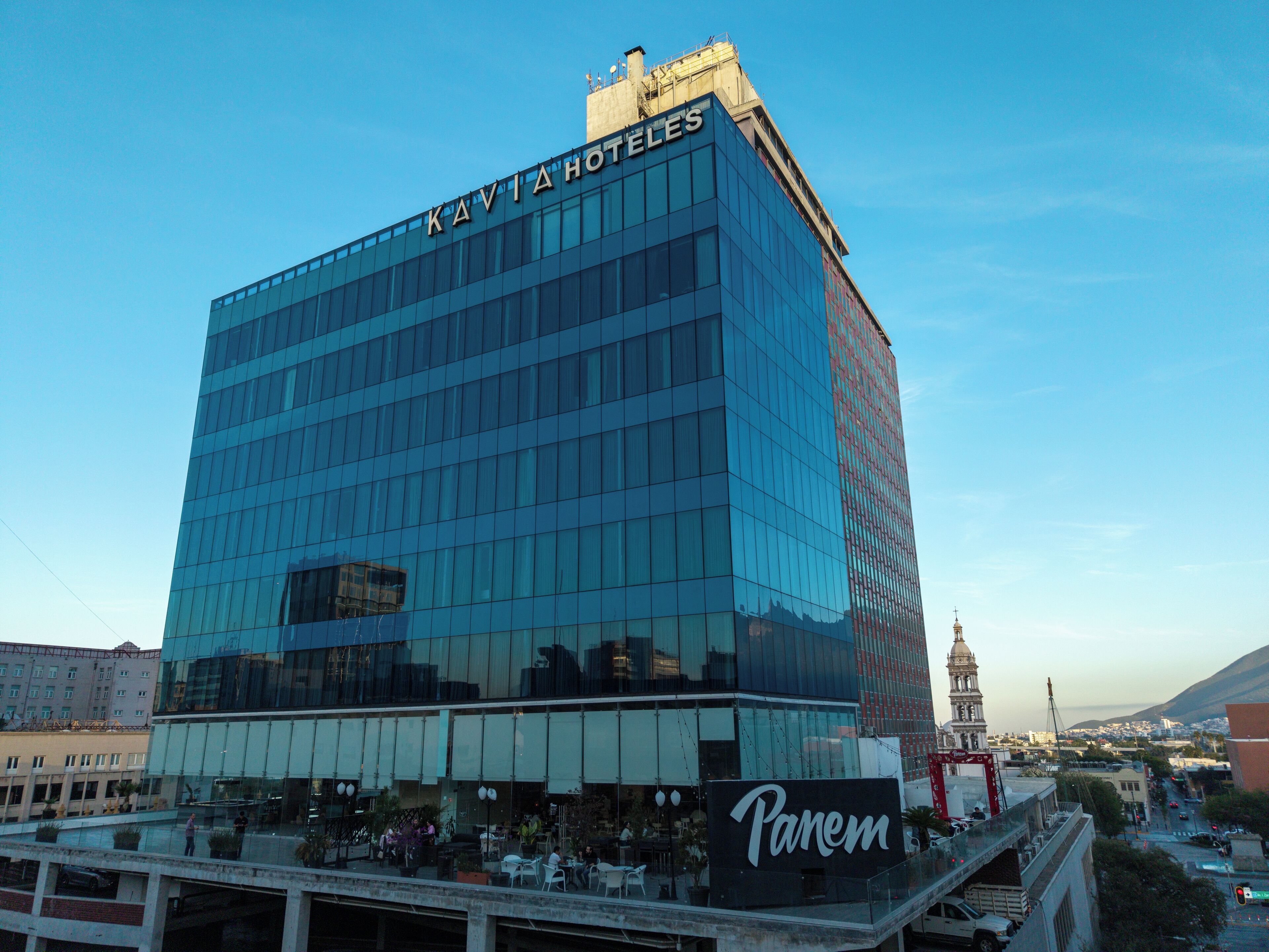 A modern hotel with a glass facade, named "KAVIAHOTELS," featuring a prominent "Panem" sign on the ground floor.