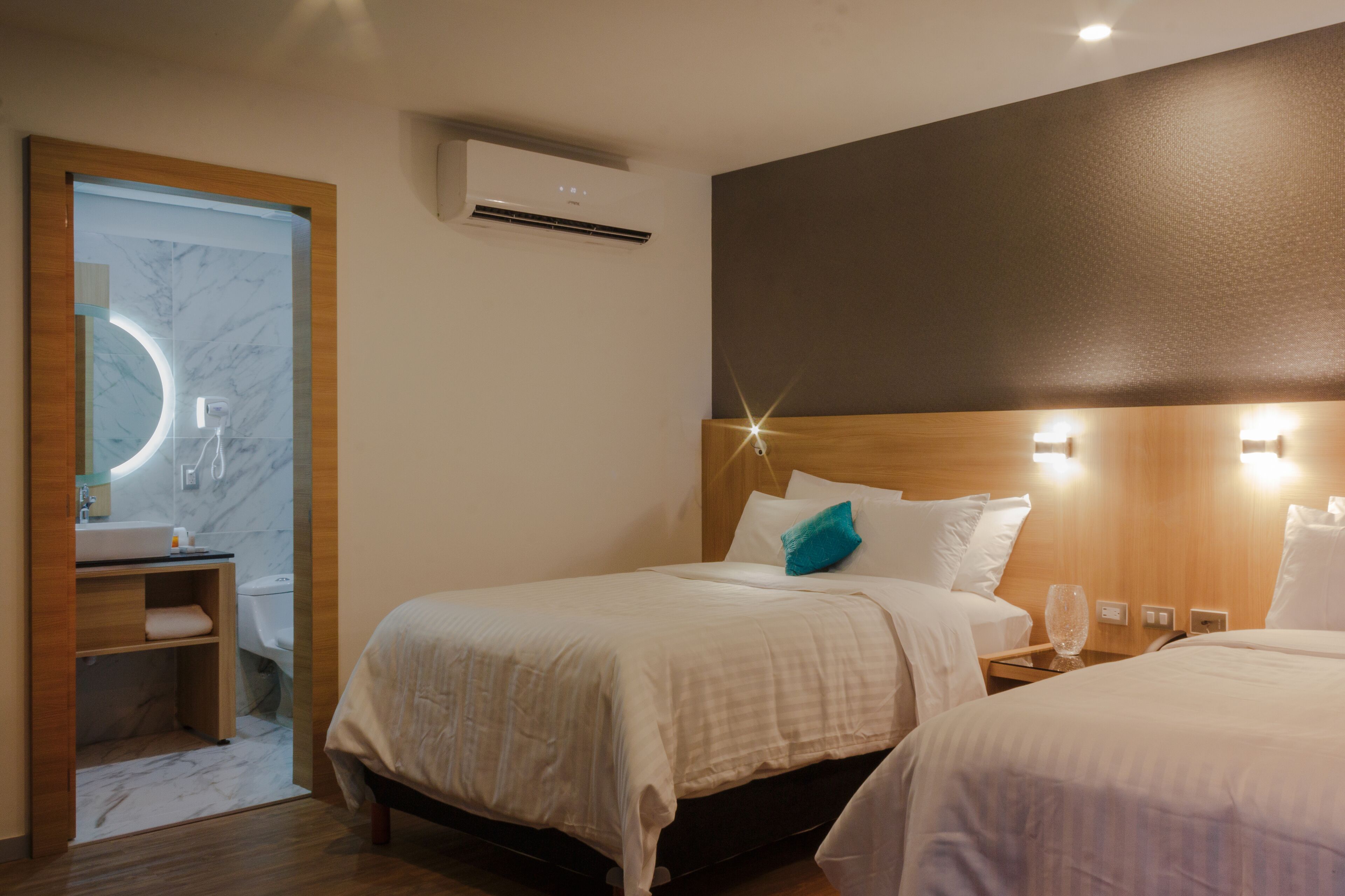 A hotel room with a bed, bedside table, and a bathroom with a mirror and sink.