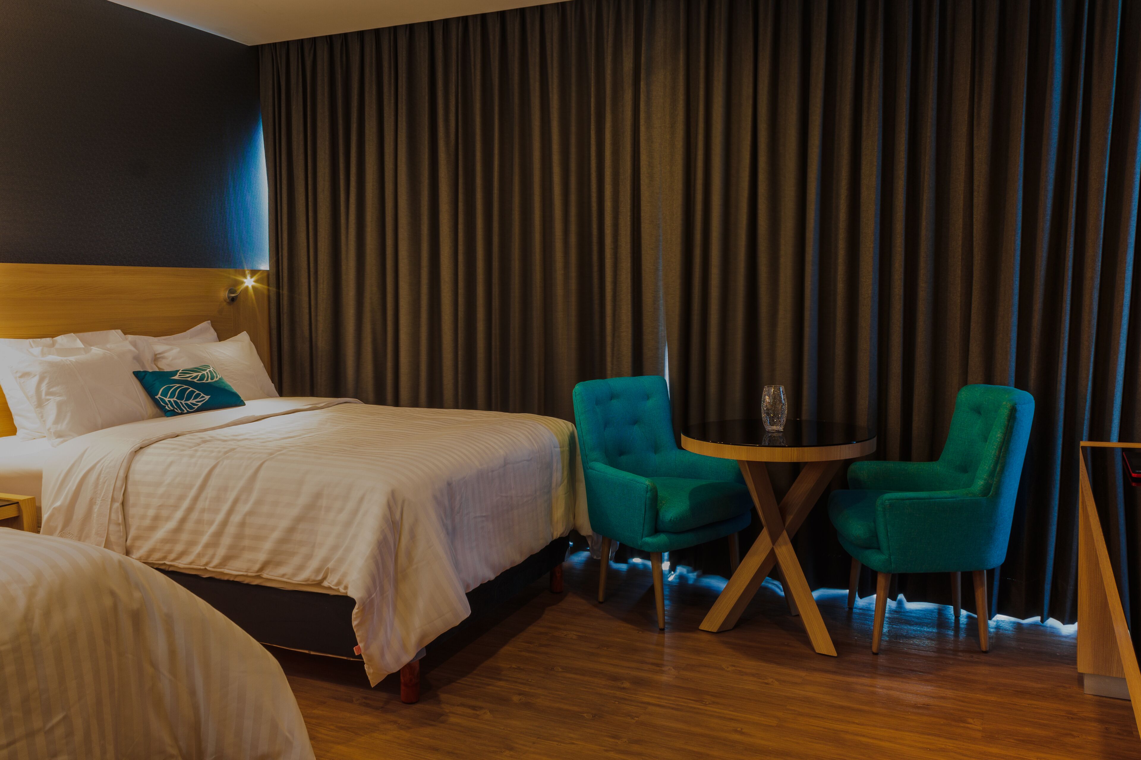 Une chambre d’hôtel avec un lit, deux chaises, une petite table et un rideau.