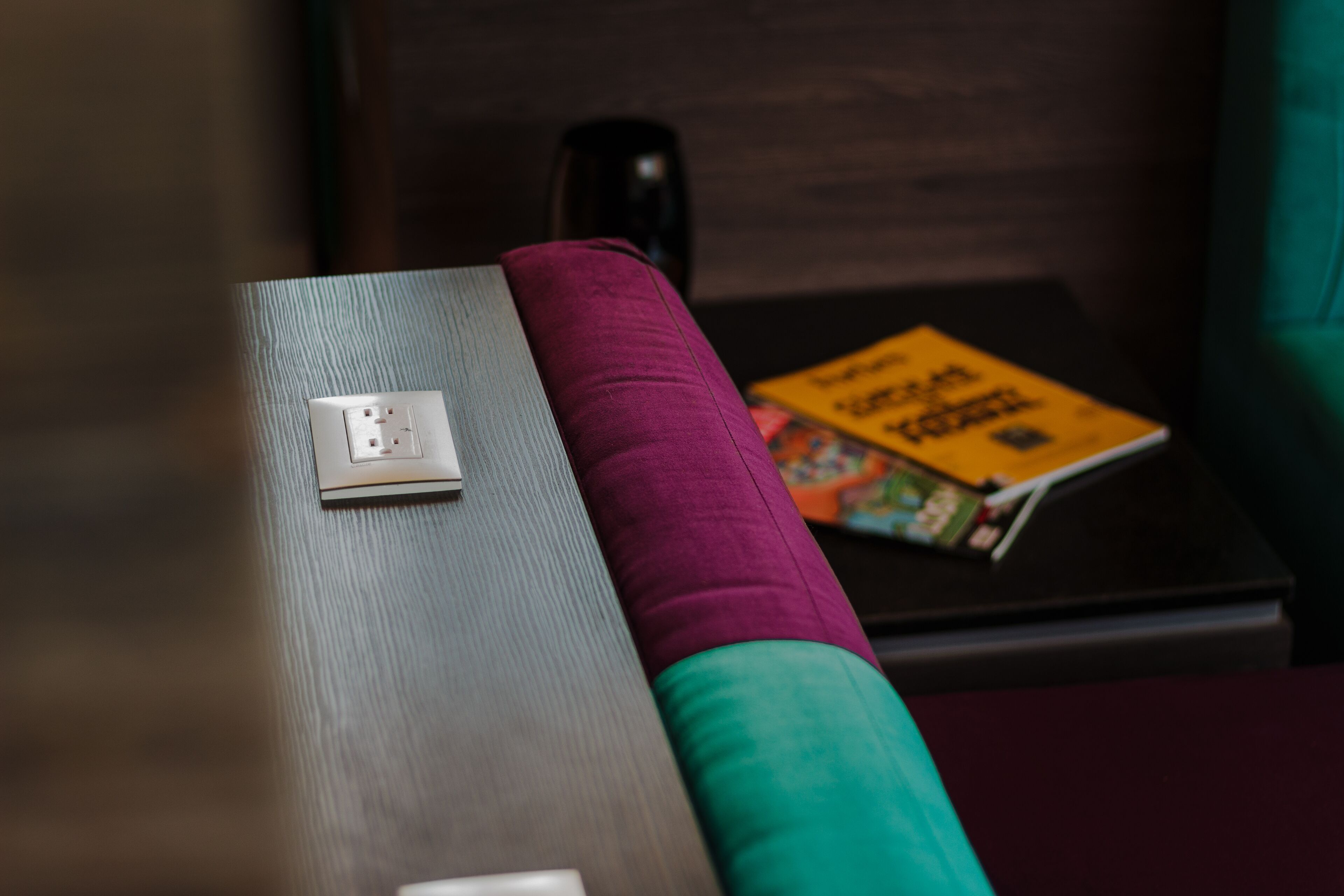 Ein Holztisch mit Steckdose, ein violettes Kissen und ein Buch auf einem kleinen schwarzen Tisch.