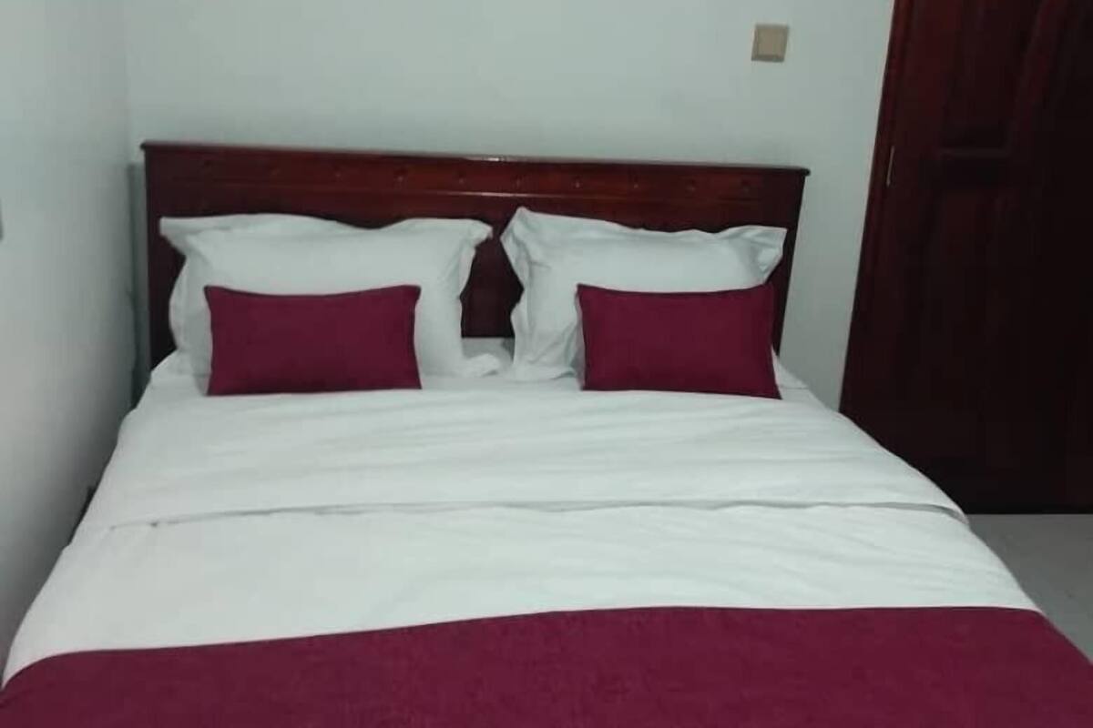 A single bed with a wooden headboard, white and maroon bedding, and a closed door to the right.