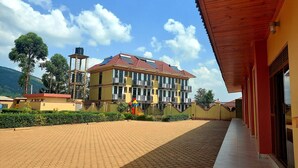 A multi-story building with a red-tiled roof, a covered walkway, and a landscaped area with a fountain. - Golden View Hotel Ibanda (Ibanda)