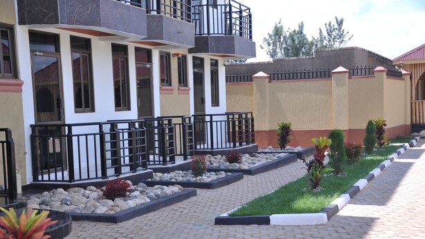 A multi-story building with balconies, a paved walkway, and landscaped areas with rocks and plants. - Golden View Hotel Ibanda (Ibanda)