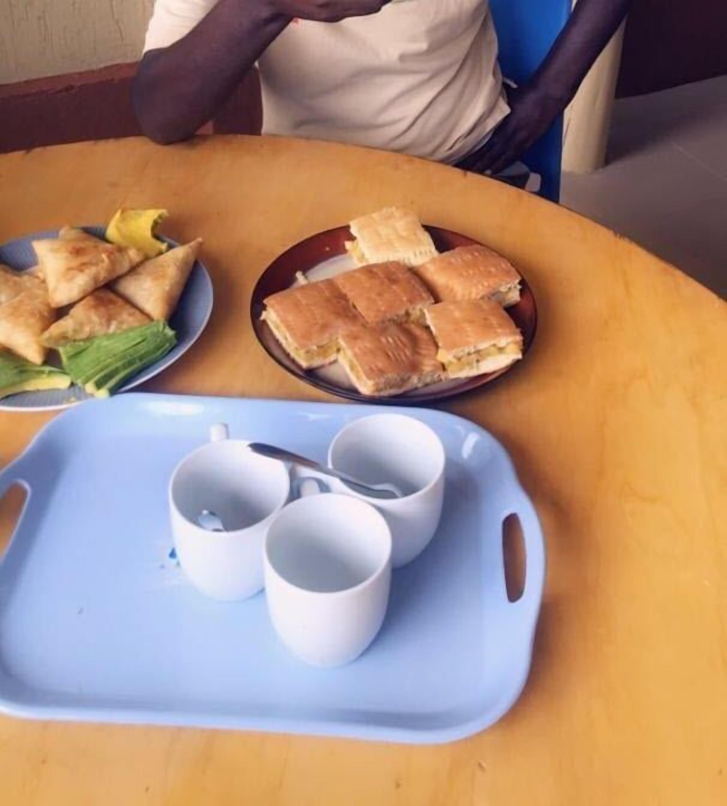 A table with a tray containing two white cups and a plate with sandwiches and a side of greens.