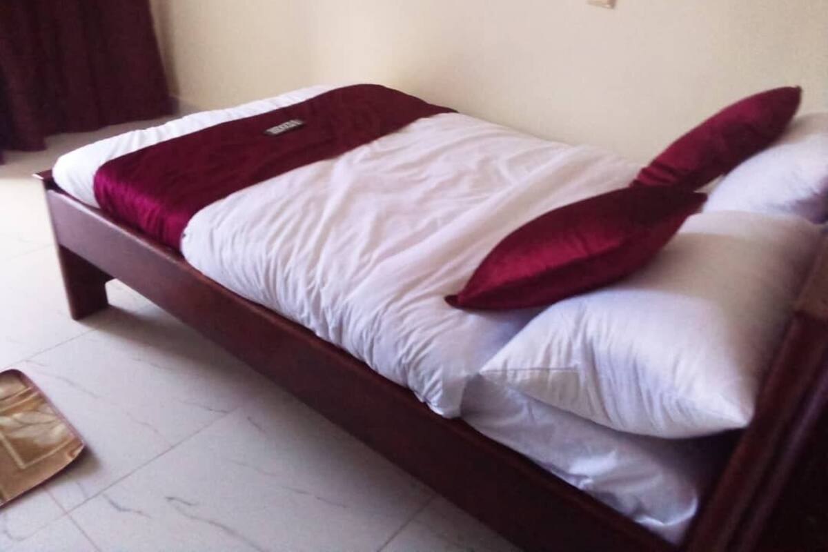 A single bed with a wooden frame, white bedding, and red pillows.