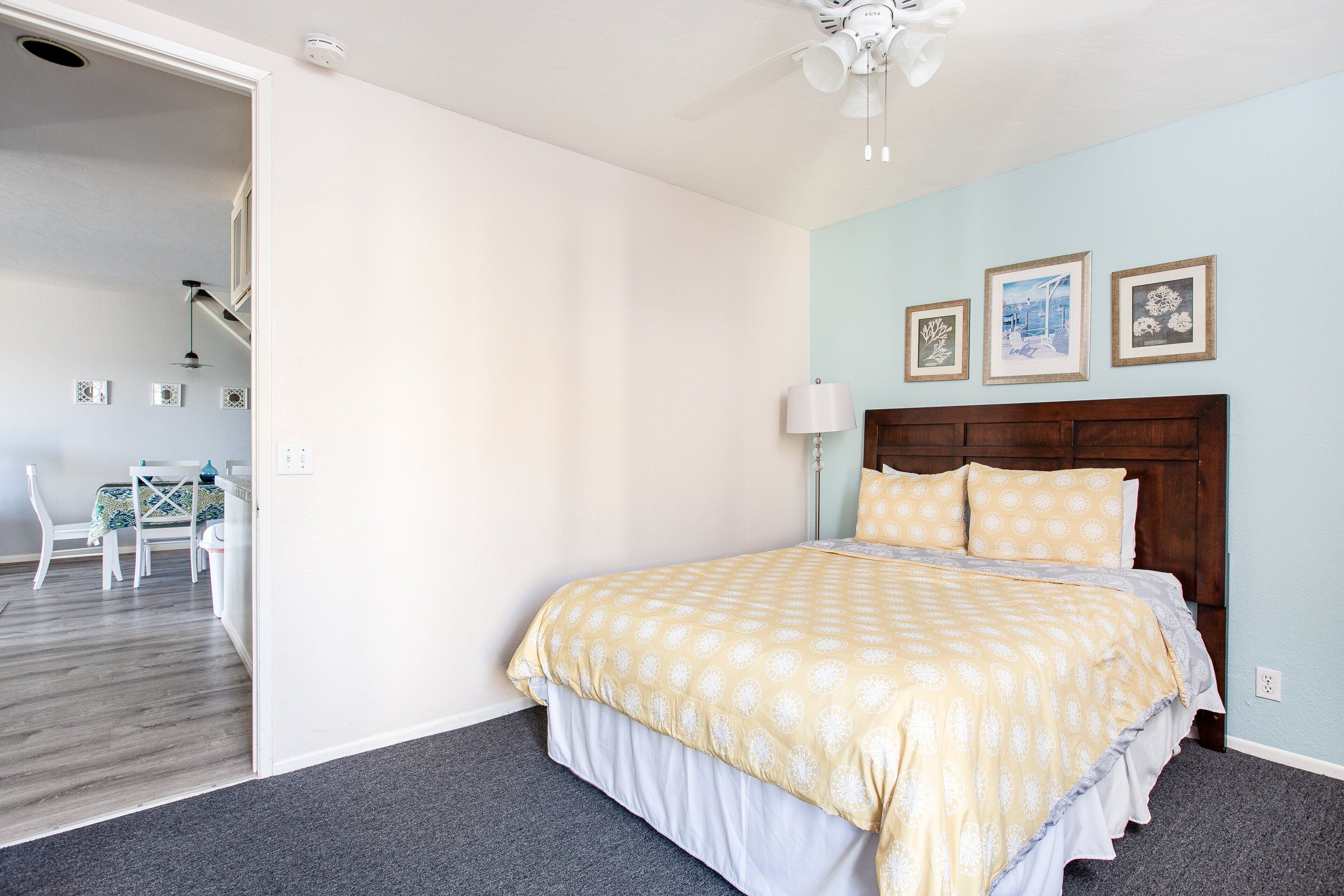 A bedroom with a bed, a wooden headboard, a nightstand, a lamp, and a wall with three framed pictures.