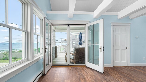 A room with large windows, a sliding glass door leading to a balcony, and a wooden floor. - Panoramic Ocean View, 5 BR, Central Air, 10 minute walk to Scarborough Beach (Narragansett)