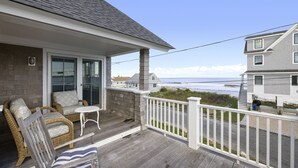 A wooden deck with wicker furniture, a small table, and a white railing overlooking a beach. - Panoramic Ocean View, 5 BR, Central Air, 10 minute walk to Scarborough Beach (Narragansett)