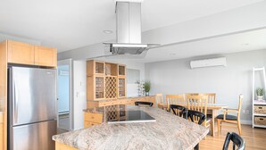 A modern kitchen with a stainless steel refrigerator, wooden cabinets, a granite countertop, and a dining area with chairs and a table. - Panoramic Ocean View, 5 BR, Central Air, 10 minute walk to Scarborough Beach (Narragansett)