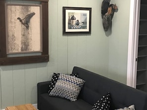 Ein Wohnzimmer mit einem dunkelgrauen Sofa, gemusterten Kissen, einem gerahmten Bild von einem Vogel und einem gerahmten Bild von einer Ente.