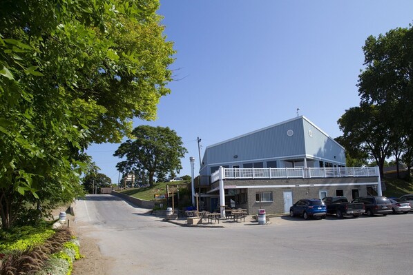 A two-story building with a balcony, parking lot, and a hillside in the background.