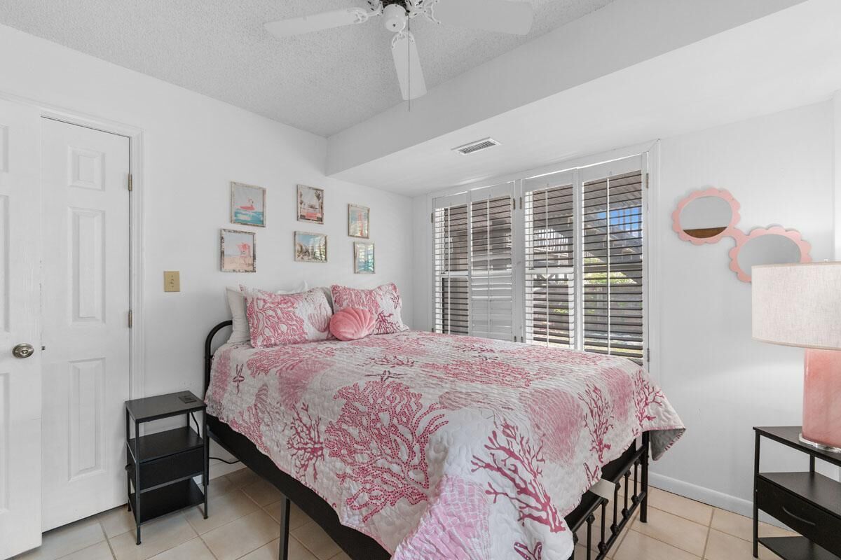 Un dormitorio con cama, ventilador de techo, ventana con persianas y decoración en las paredes.