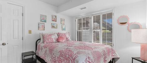 Un dormitorio con cama, ventilador de techo, ventana con persianas y decoración en las paredes.