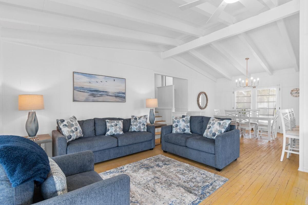 A spacious living room with two sofas, a coffee table, and a rug. There is a dining area with a white table and chairs.