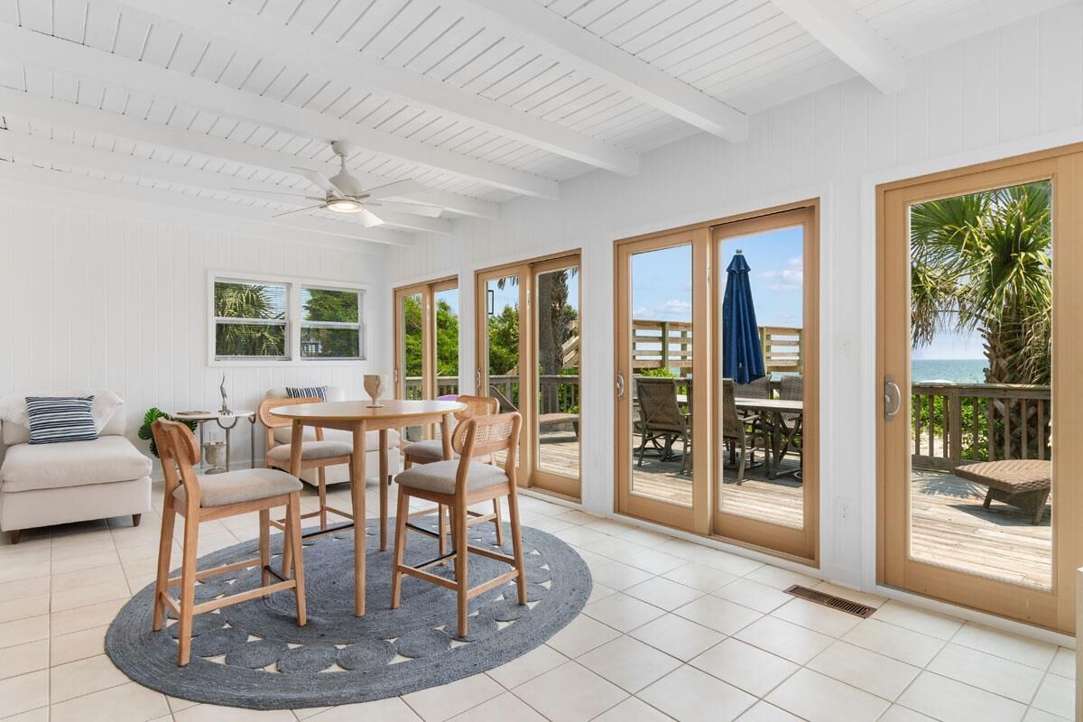 A spacious room with a round table and chairs, a ceiling fan, and large sliding glass doors leading to an outdoor deck with a view of the ocean.