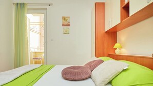 A neatly made bed with green and white bedding, a wooden wardrobe, and a small table with a lamp. - Apartments Zelic Tucepi  S3 (Tucepi)