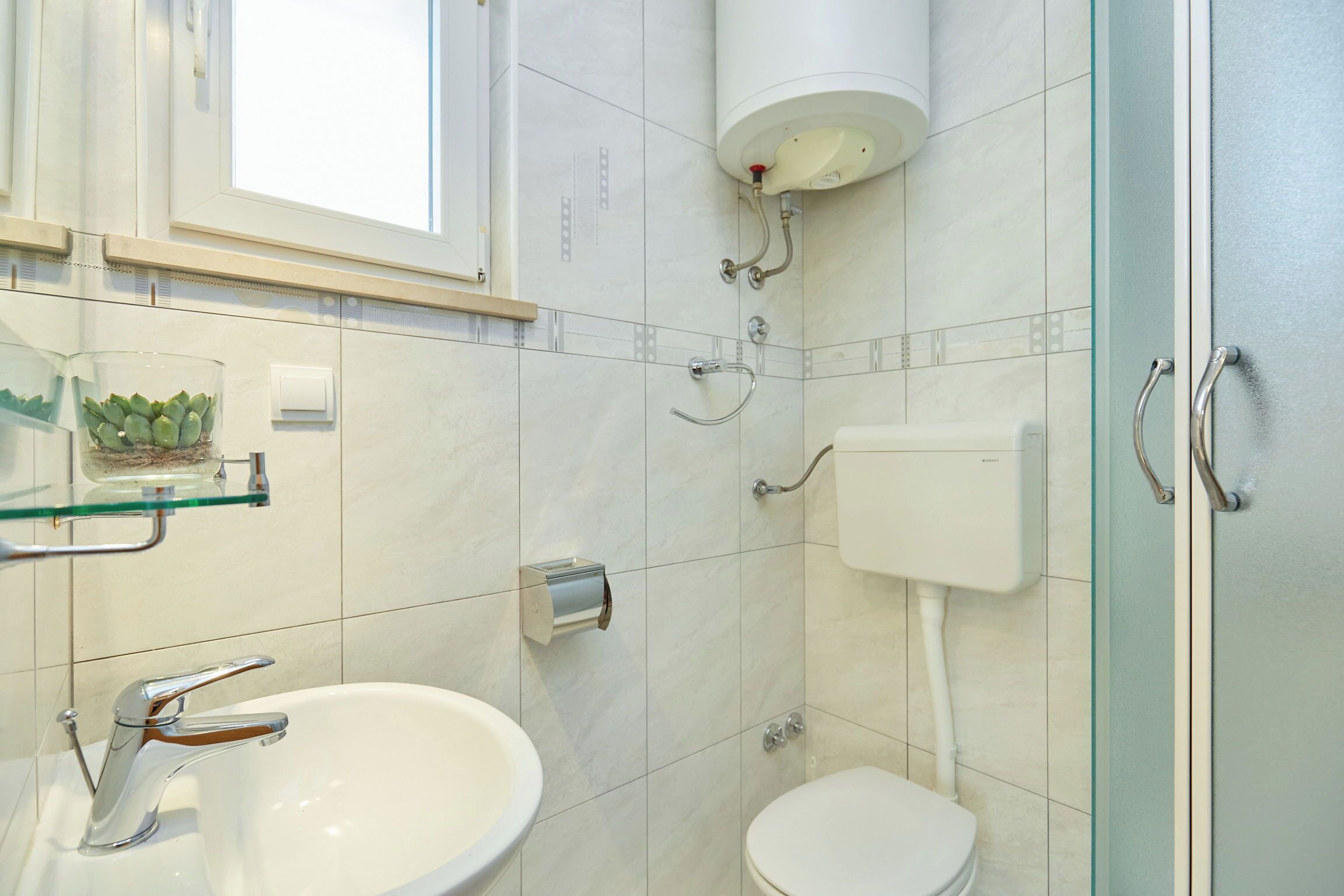 A modern bathroom with a glass shower enclosure, a white toilet, and a sink with a chrome faucet.