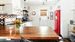 Una cocina moderna con una isla de madera, armarios blancos, un refrigerador rojo y un ventilador de techo.