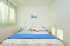 A bedroom with a bed, two bedside tables, a window with curtains, and a framed picture on the wall.