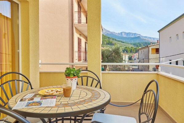 A round table with chairs on a balcony, a potted plant, and a glass of beverage.