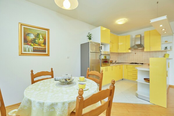 A compact kitchen with yellow cabinets, a refrigerator, and a dining area with a table and chairs.