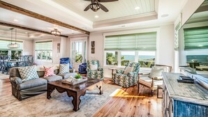 A spacious living room with a high ceiling, wooden flooring, and large windows offering a view of the ocean. - Creekfront Home with Pool, Dock and Stunning Views (Pawleys Island)