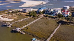 An aerial view of a coastal property with multiple buildings, a beach, and a boardwalk leading to docks. - Creekfront Home with Pool, Dock and Stunning Views (Pawleys Island)