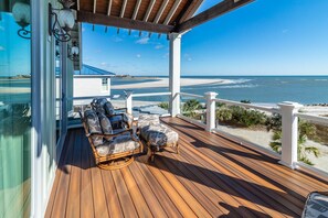 A wooden deck with wicker furniture and a view of the beach.