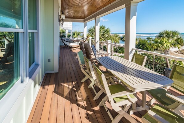 A covered outdoor area with wooden deck, seating, and a view of the beach.